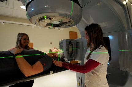 THE GIRLS: Radiation therapists Carolina Morena (on the table), Danielle Midgette (left) and Kristina Howell (right) show visitors what the linear accelerator looks like in action.