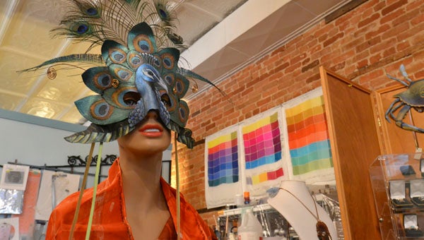 VAIL STEWART RUMLEY | DAILY NEWS THE SETUP: The eyes behind one of Doris Schneider’s masks watches over the preparations for Monday’s opening at Lemonade Art Gallery in downtown Washington. In the background is silk artist Jan Lamoreaux who joins four other artists from Inner Banks Artisans’ Center in opening the new West Main Street gallery. 