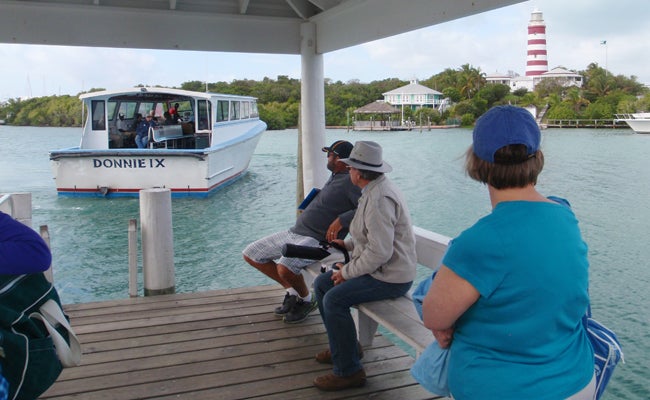 FRED BONNER | CONTRIBUTED PHOTO OPP: The inter-island ferry “Donnie IX” backs up to the lower dock at Hope Town. In the background is the historic Elbow Reef Lighthouse, the most photographed spot in the Abacos.