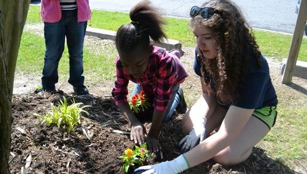 JONATHAN ROWE LANDSCAPING: Wednesday, in accordance with Earth Day, employees with U.S. Cellular met with members of Washington’s Boys and Girls Club to plant flowers, pick weeds and water new and existing flora. Pictured (left to right) are Ka’mayah Freeman, a fourth-grade student at John Small Elementary, Reagan Ruther, a sixth-grade student at P.S. Jones Middle School as they watch an example of the process of planting a flower by U.S. Cellular associate Jamiyan Phillips. 